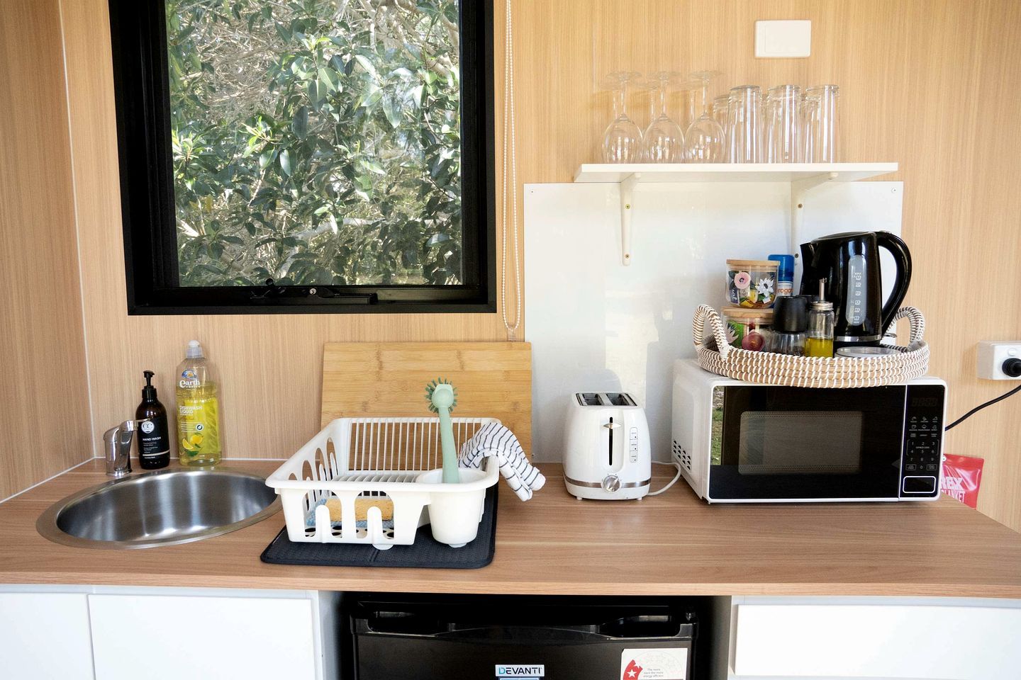 Cocina compacta con lavamanos, tostadora, microondas y ventana con vistas a la vegetación.