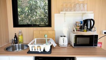 Cocina compacta con lavamanos, tostadora, microondas y ventana con vistas a la vegetación.