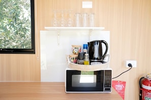 Cozinha equipada com micro-ondas, cafeteira e uma estante com copos e extintor de incêndio.