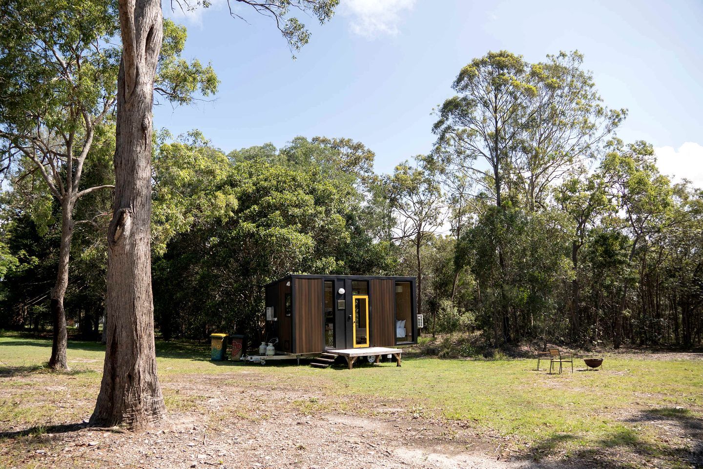 A small, single-story cabin with a wooden exterior and a yellow door, surrounded by trees in a natural setting.