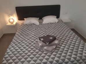 A neatly made bed with a geometric patterned bedspread, two pillows, and a stack of folded towels with star patterns. - Groundfloor Lopagan (San Pedro del Pinatar)