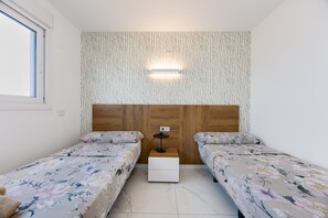 A small, well-lit room with two single beds, a wooden headboard, a nightstand, and a wall-mounted light fixture. - Apartment Valonia Punta Prima BR3 (Torrevieja)