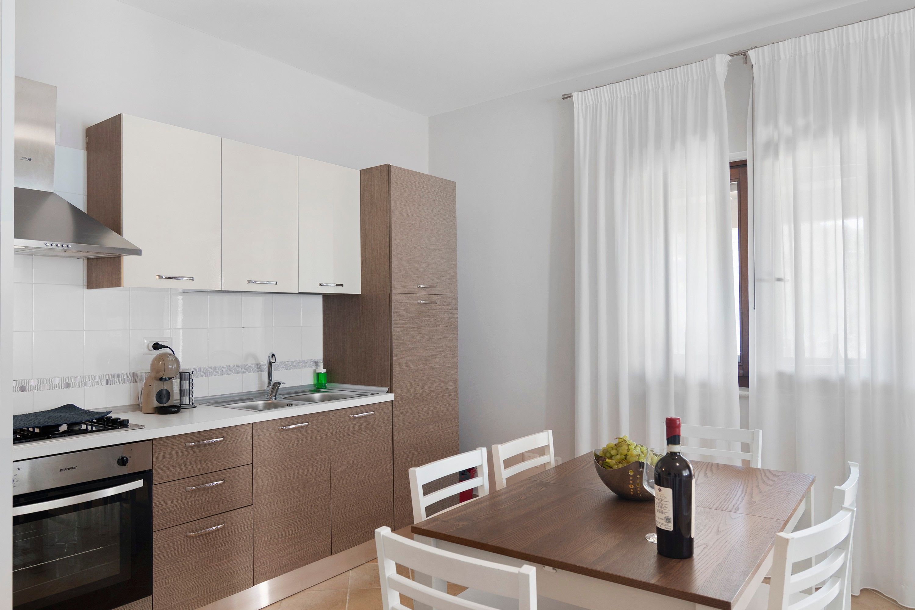 Eine moderne Küche mit weißen Schränken, einem eingebauten Backofen und einem Esstisch mit Stühlen.