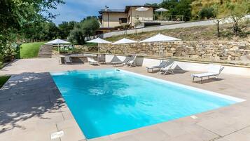 Una piscina rectangular con un muro de piedra y una casa al fondo.
