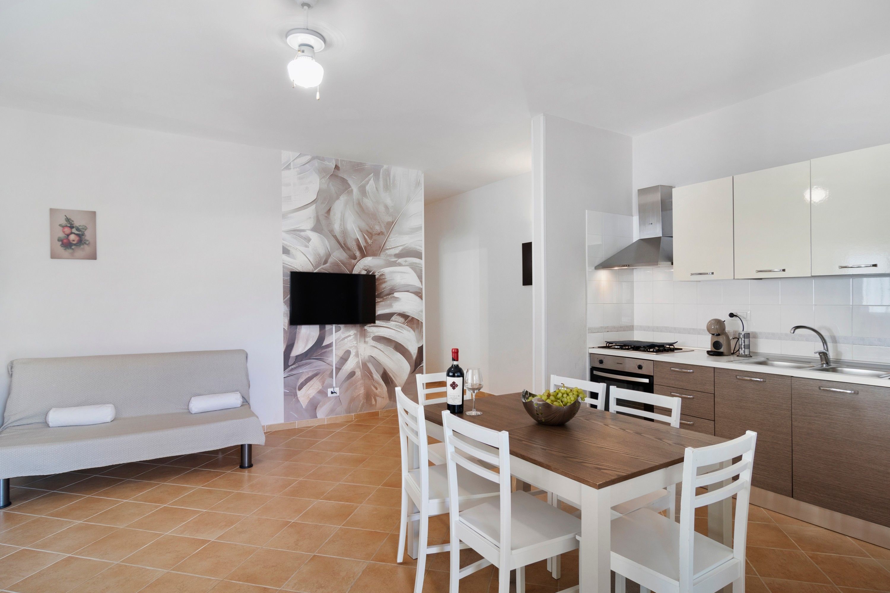 Une cuisine moderne avec des meubles blancs, une table à manger avec des chaises, un canapé et un téléviseur à écran plat fixé au mur.