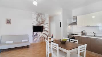 Una cucina moderna con mobili bianchi, un tavolo da pranzo con sedie, un divano e una TV a schermo piatto montata a parete.