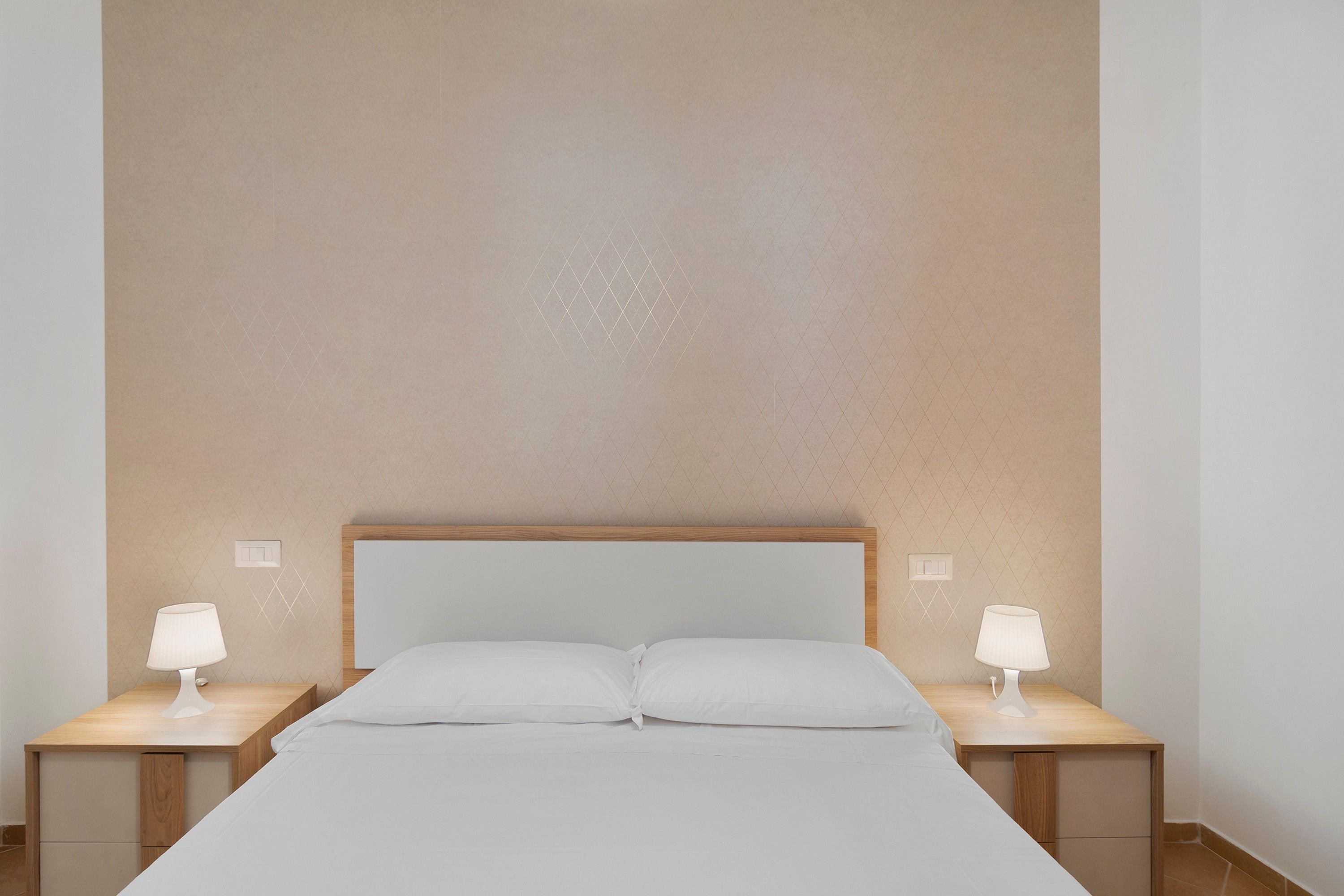 A hotel room with a large bed, two bedside tables, and two wall-mounted lamps.