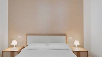 A hotel room with a large bed, two bedside tables, and two wall-mounted lamps.