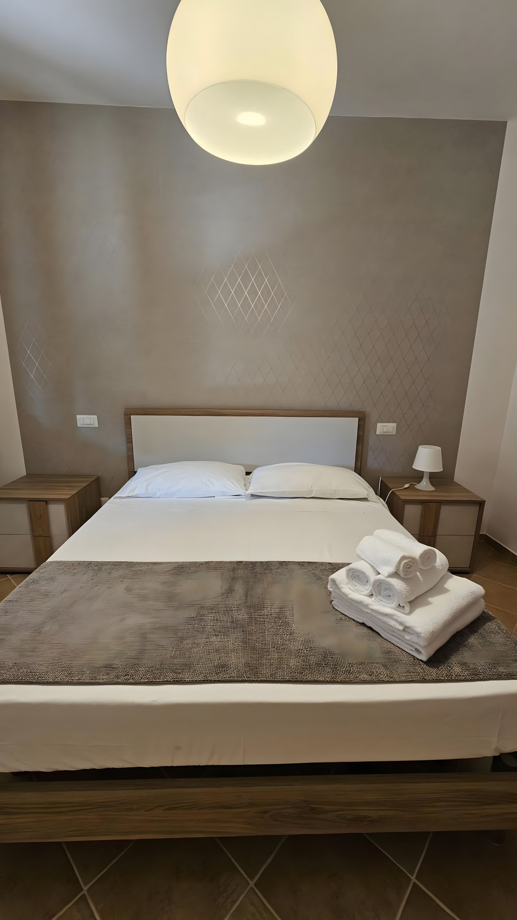 A neatly made bed with a headboard, two bedside tables with lamps, and a large ceiling light.