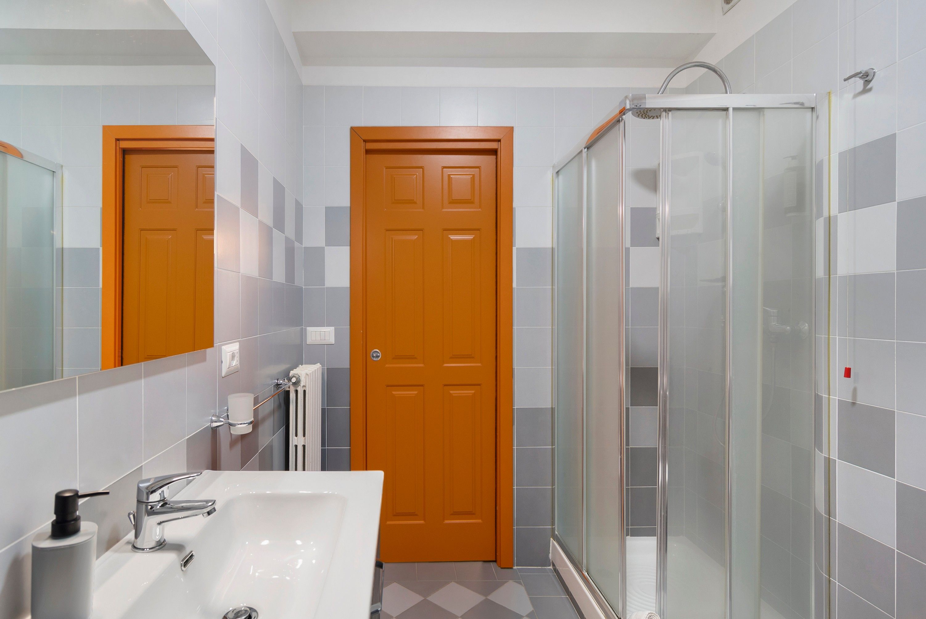 A bathroom with a white sink, a glass shower enclosure, and a wooden door.