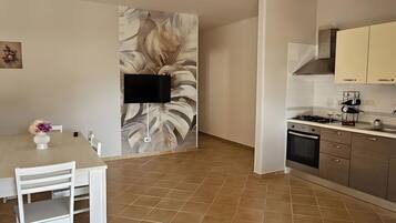 Een ruime woonkamer met een eettafel, stoelen, een plafondventilator, en een keuken met kastjes en een fornuis.