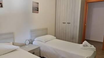 A hotel room with two beds, a wardrobe, a nightstand, and a hanging light fixture.
