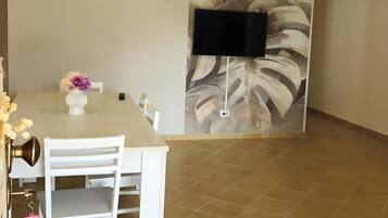 Un coin repas comprenant une table, des chaises, un vase de fleurs, un ventilateur de plafond et un téléviseur fixé au mur.