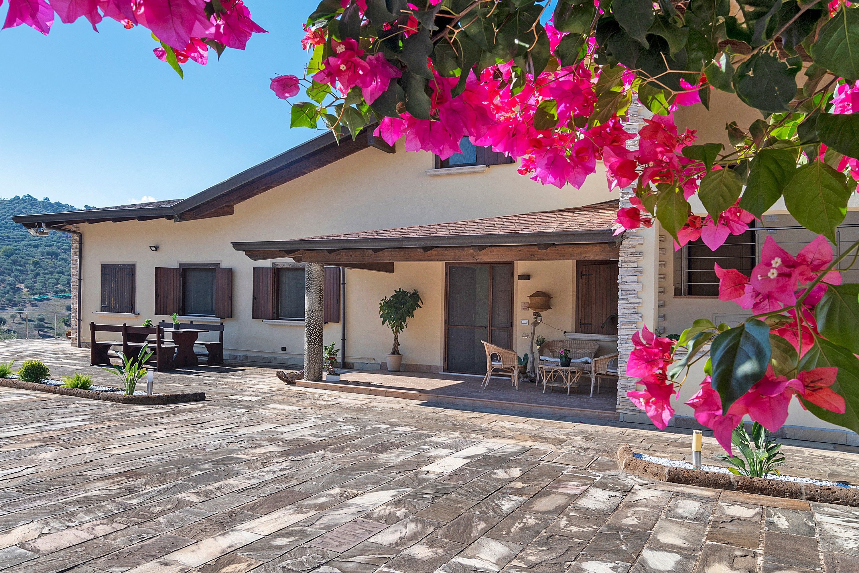 Una casa con un patio, mobiliario exterior y flores de buganvilla.