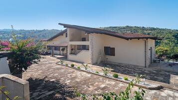A two-story building with a flat roof, stone pillars, and a paved courtyard with plants.