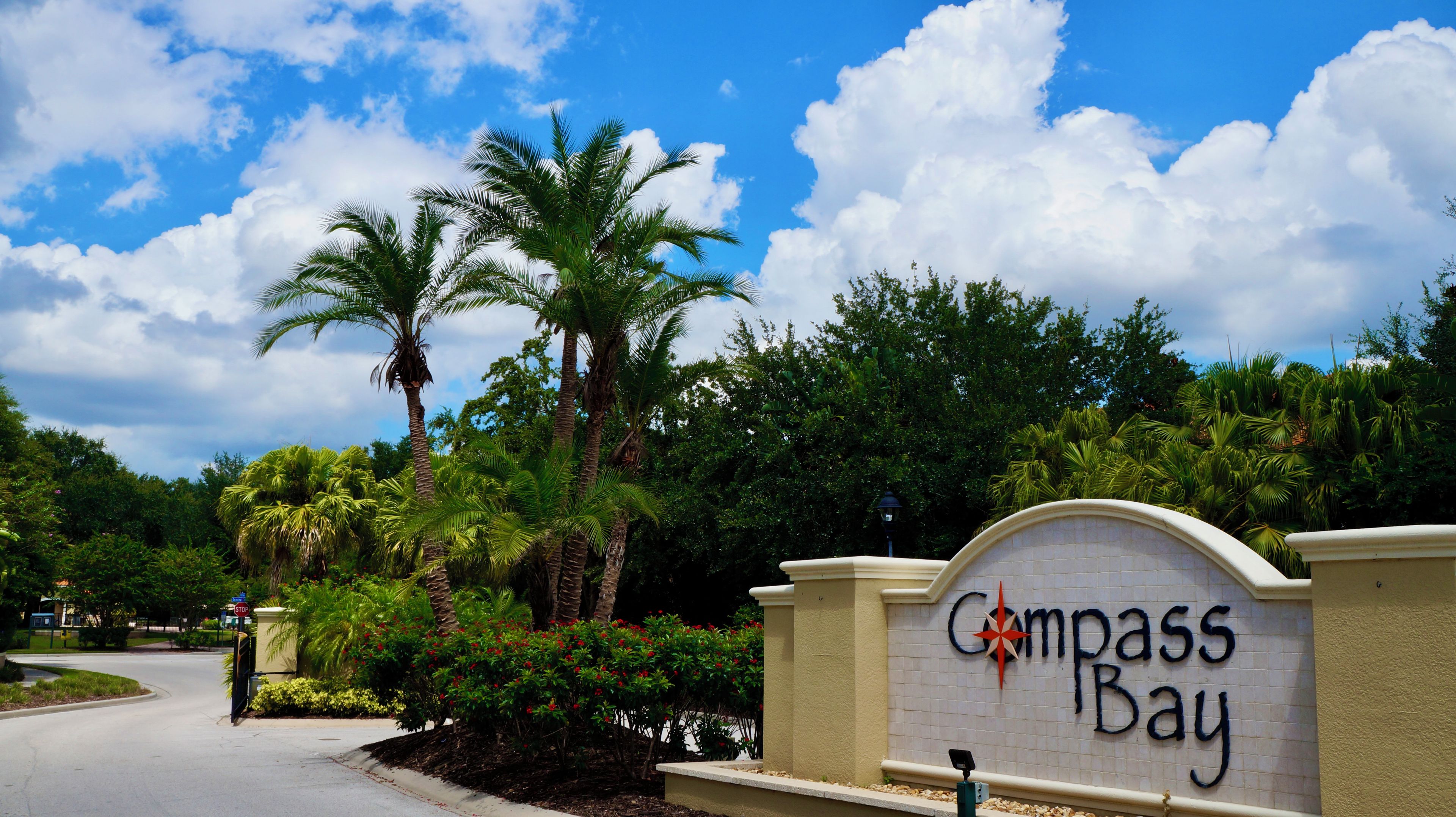 A sign for Compass Bay with palm trees and a clear sky in the background.
