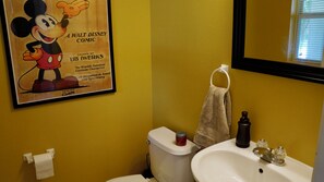 Een badkamer met een Mickey Mouse stripverhaal poster, een toilet, een wastafel en een handdoekhouder.