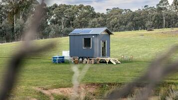 A small, single-story cabin with a sloped roof, solar panels, and a clear view of the surrounding landscape.