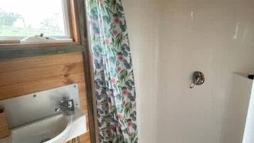 Une salle de bain avec un plafond en bois, un lavabo blanc, une douche avec un rideau à motifs floraux et une fenêtre.