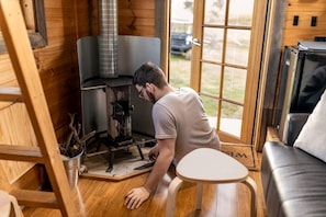 Una persona operando un horno de leña en una cabaña con vistas al exterior.