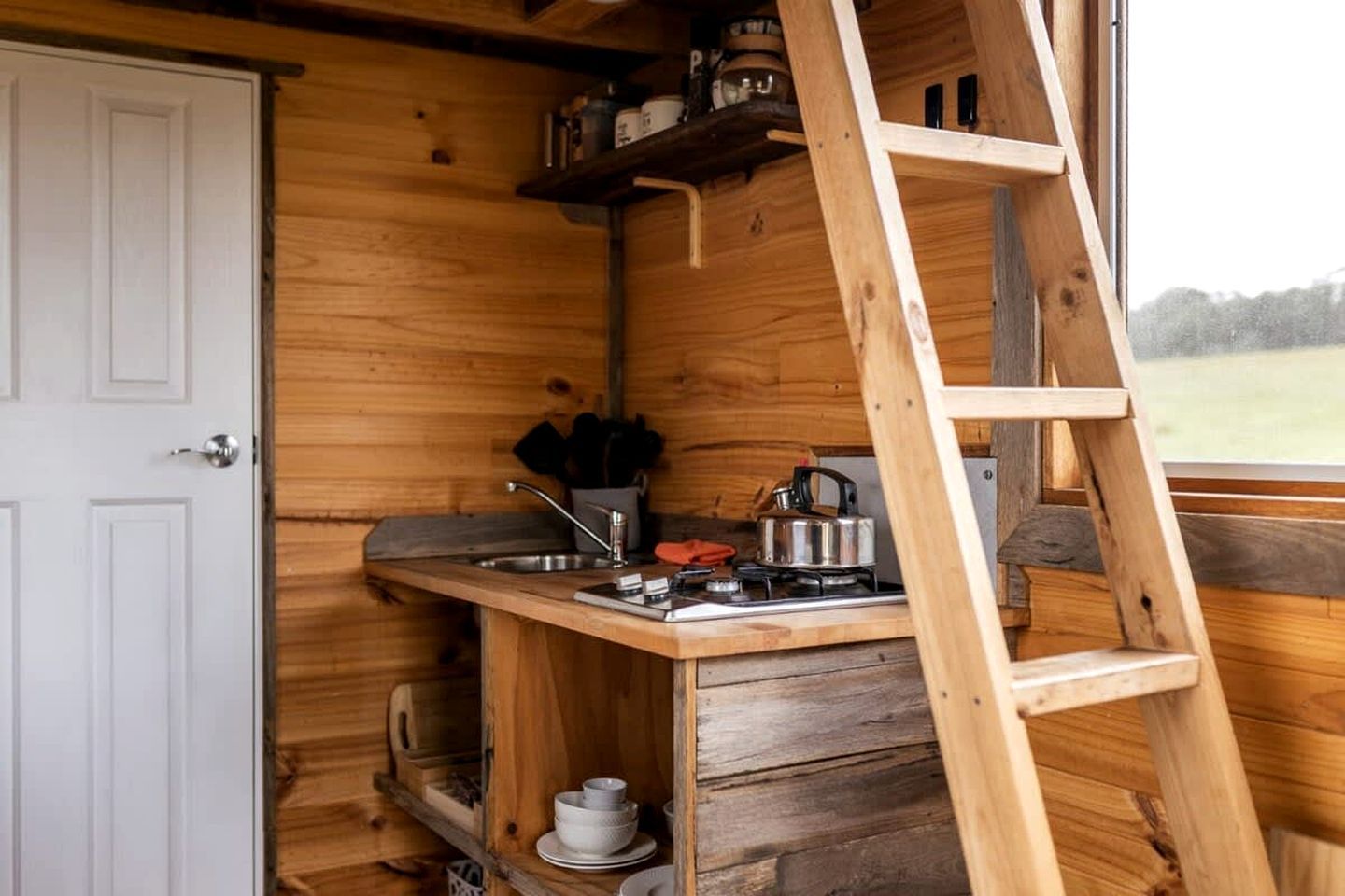 A compact kitchen with a wooden interior, a sink, a stove, and a ladder.