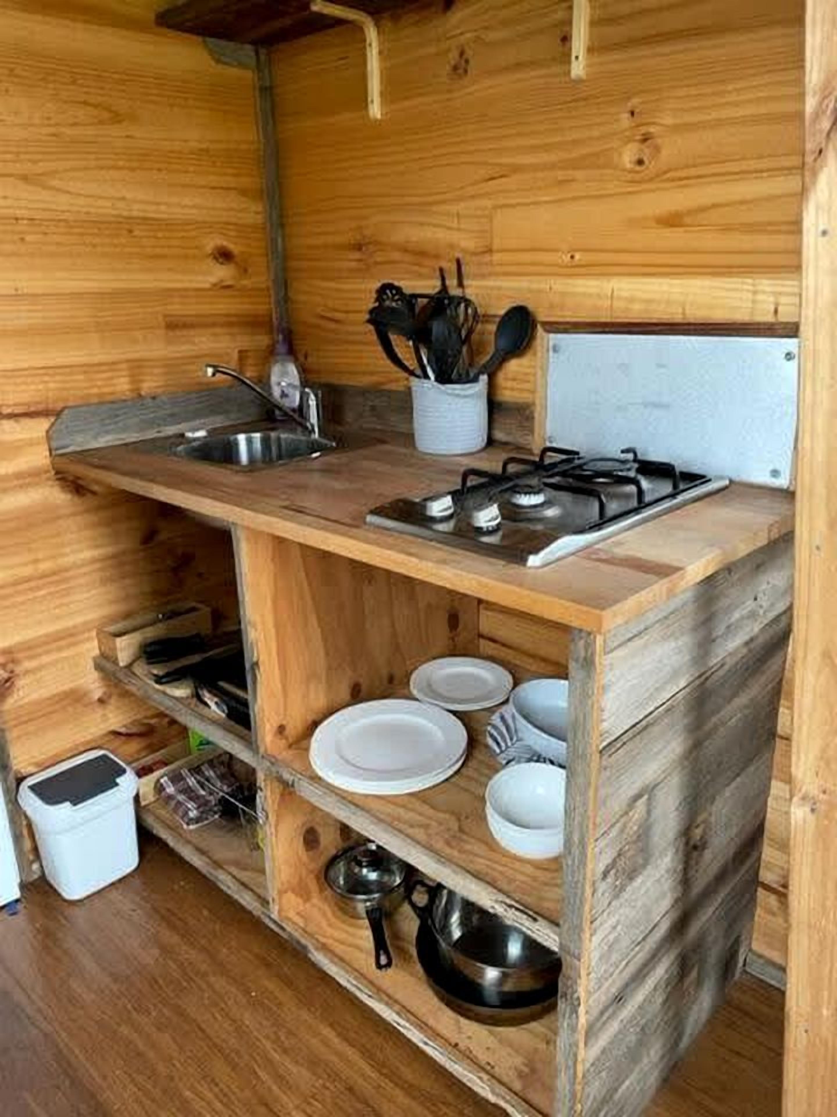 A compact wooden kitchen with a sink, stove, and shelves for dishes and cookware.