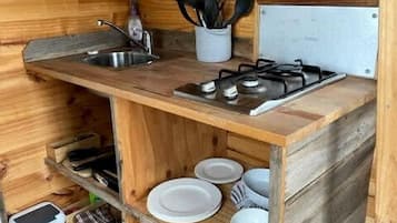 A compact wooden kitchen with a sink, stove, and shelves for dishes and cookware.
