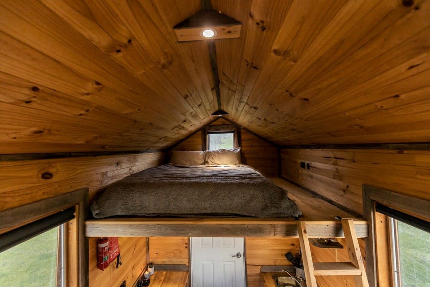 Eine kleine Holzhütte mit Schlafzimmer auf dem Dachboden, einem Fenster und einer Leiter.