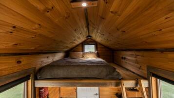 Eine kleine Holzhütte mit Schlafzimmer auf dem Dachboden, einem Fenster und einer Leiter.
