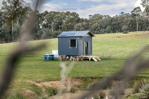 A small, single-story cabin with a sloped roof, solar panels, and a clear view of the surrounding landscape.