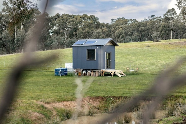 Una cabaña pequeña de un piso con techo inclinado, paneles solares y una vista despejada del paisaje circundante.