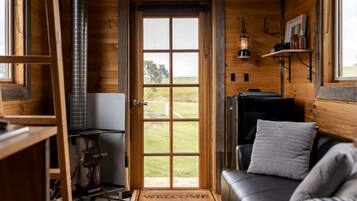 A cozy cabin interior with a wooden door leading to a view, a fireplace, a sofa, and a small table with a lantern.