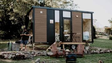 A compact wooden structure with a deck, outdoor seating, and a person working on a tool.