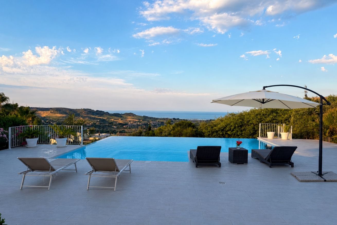 A swimming pool with lounge chairs and an umbrella, overlooking a scenic landscape.