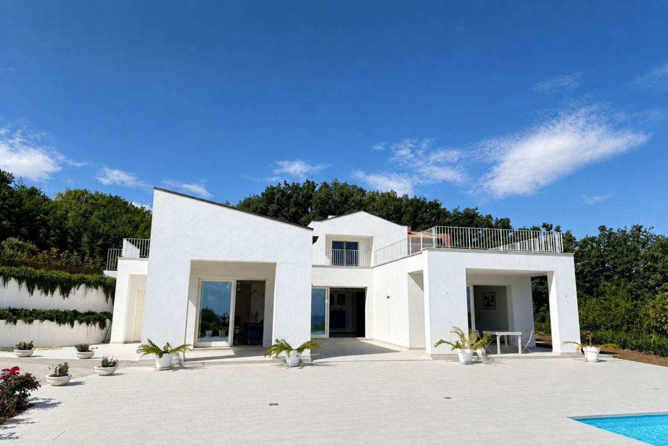 Une maison moderne à deux étages avec une piscine, entourée de verdure et sous un ciel dégagé.
