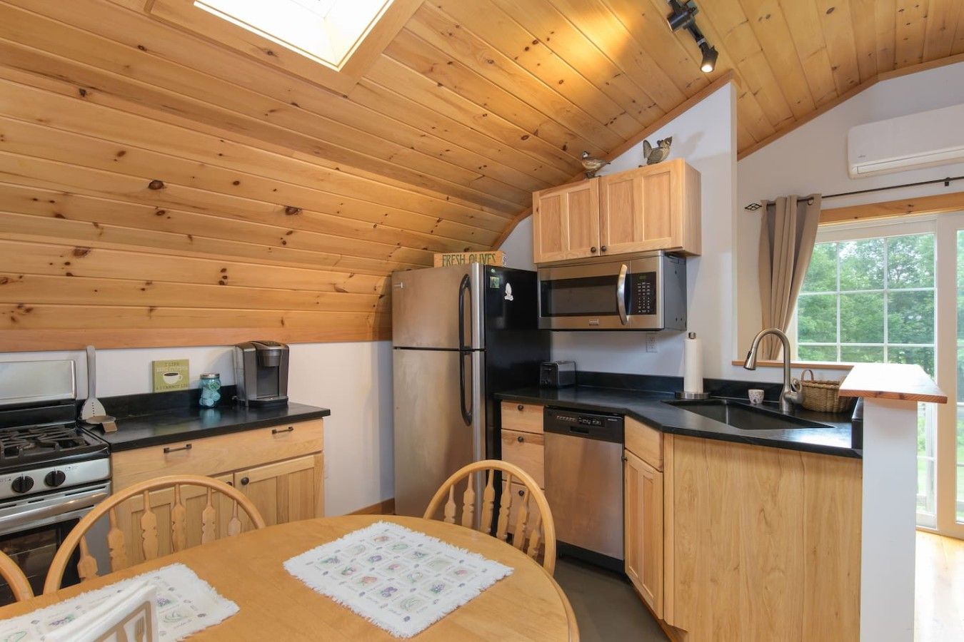 Une cuisine compacte dotée de meubles en bois, d’un réfrigérateur, d’un four à micro-ondes, d’une cuisinière et d’un coin repas avec une table et des chaises.