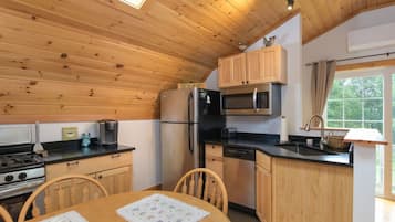 Une cuisine compacte dotée de meubles en bois, d’un réfrigérateur, d’un four à micro-ondes, d’une cuisinière et d’un coin repas avec une table et des chaises.