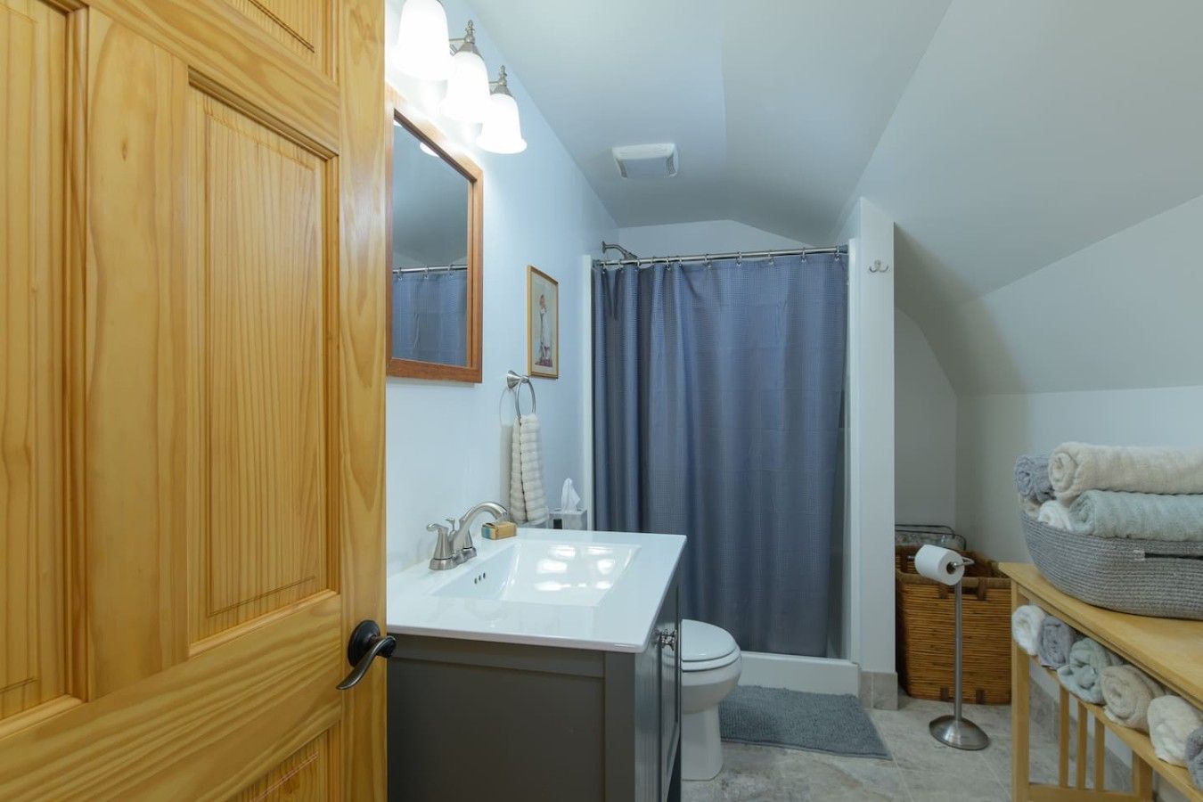 A bathroom with a wooden door, a white sink, a shower curtain, and a towel rack.
