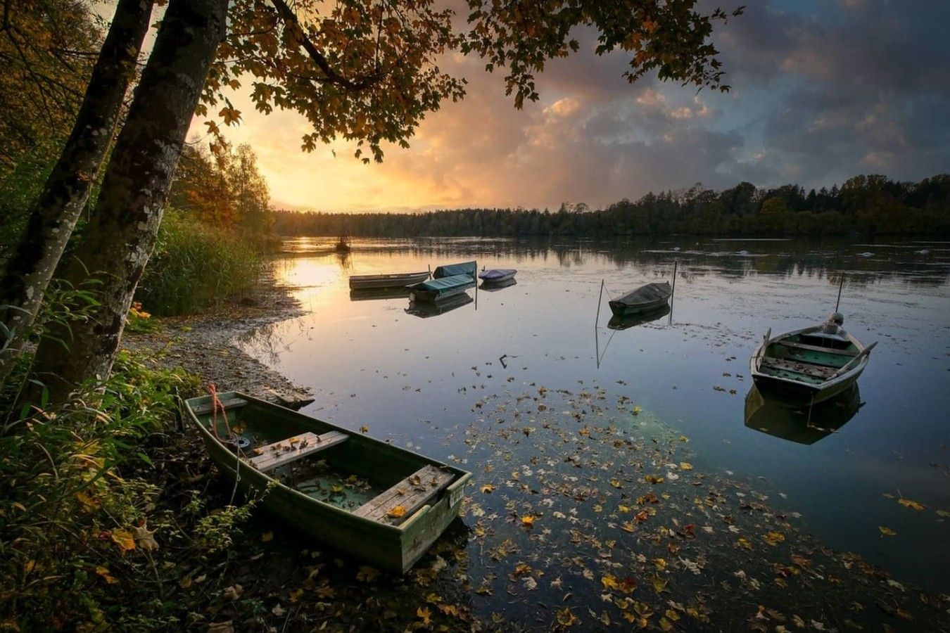 Ein ruhiger See mit Booten, Bäumen und einem Sonnenuntergang.