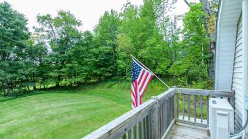 A wooden deck with a flag, surrounded by a well-maintained lawn and dense trees.