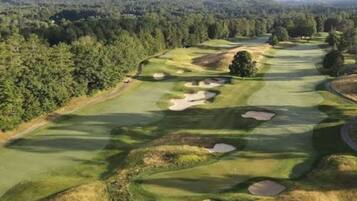 Ein Golfplatz mit Sandbunkern und einem bewaldeten Bereich.