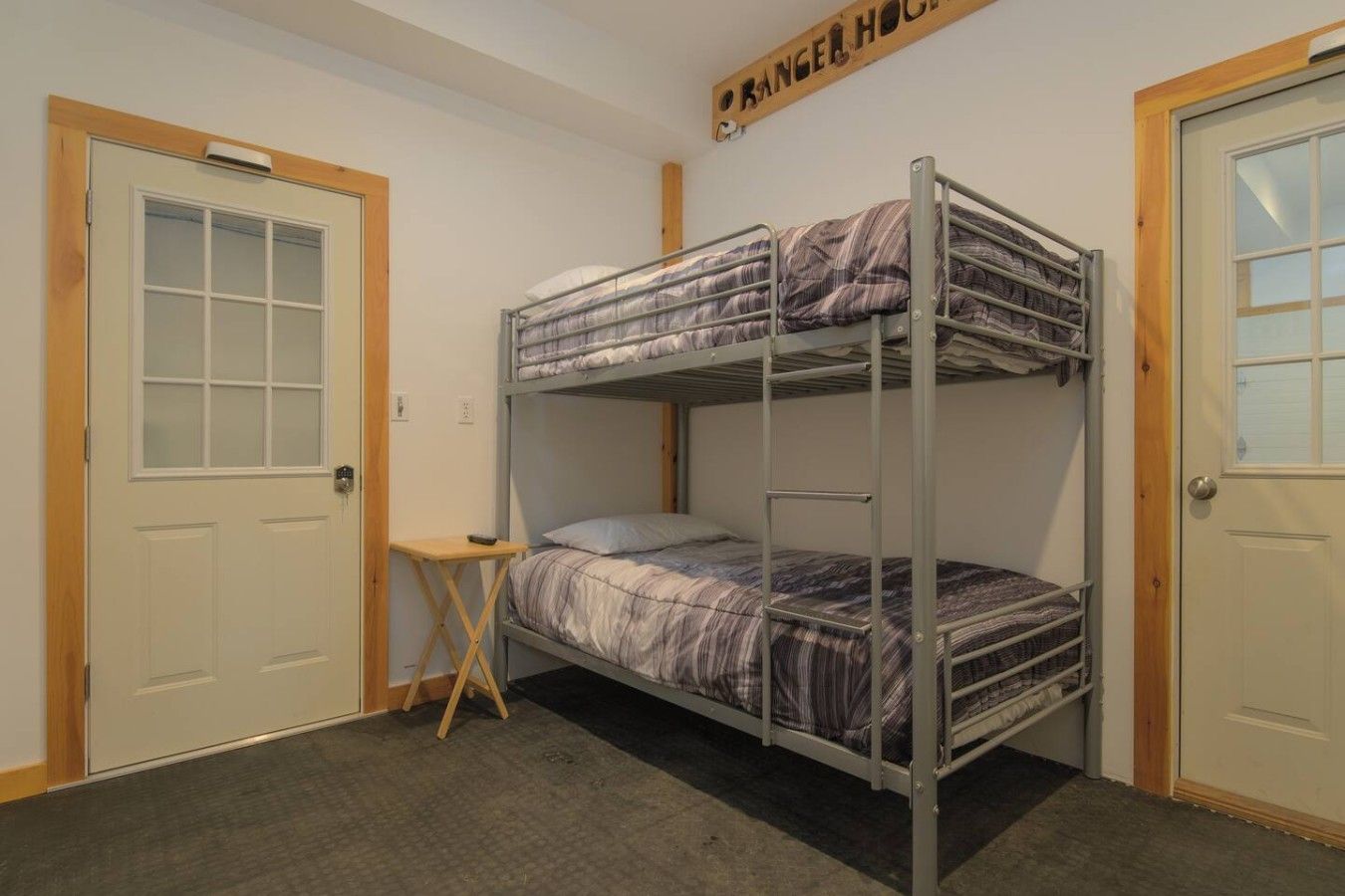 Une chambre avec des lits superposés, une petite table et une porte portant l’inscription « Maison du garde-chasse ».