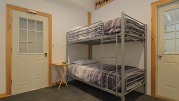 Une chambre avec des lits superposés, une petite table et une porte portant l’inscription « Maison du garde-chasse ».