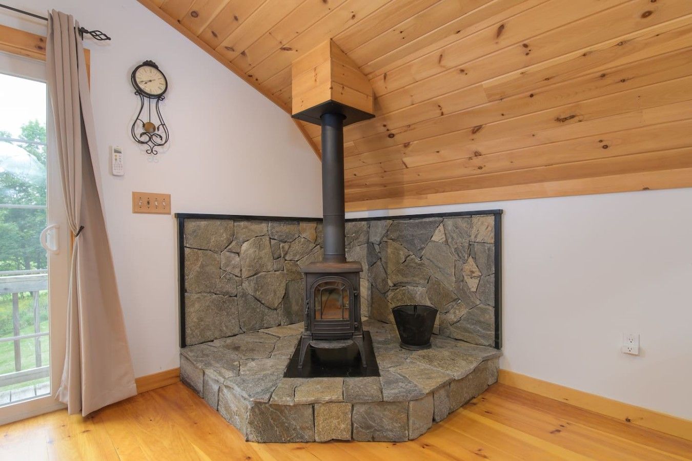 Una habitación con chimenea de piedra, techo de madera y una ventana con cortinas.