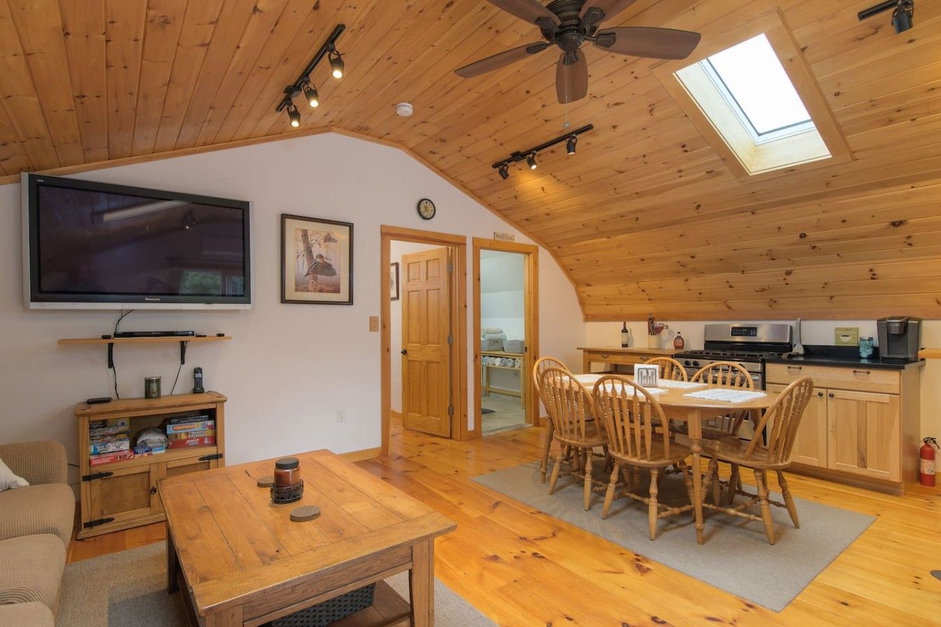 Ein gemütliches Zimmer mit Esstisch, Stühlen, Fernseher und Deckenventilator.