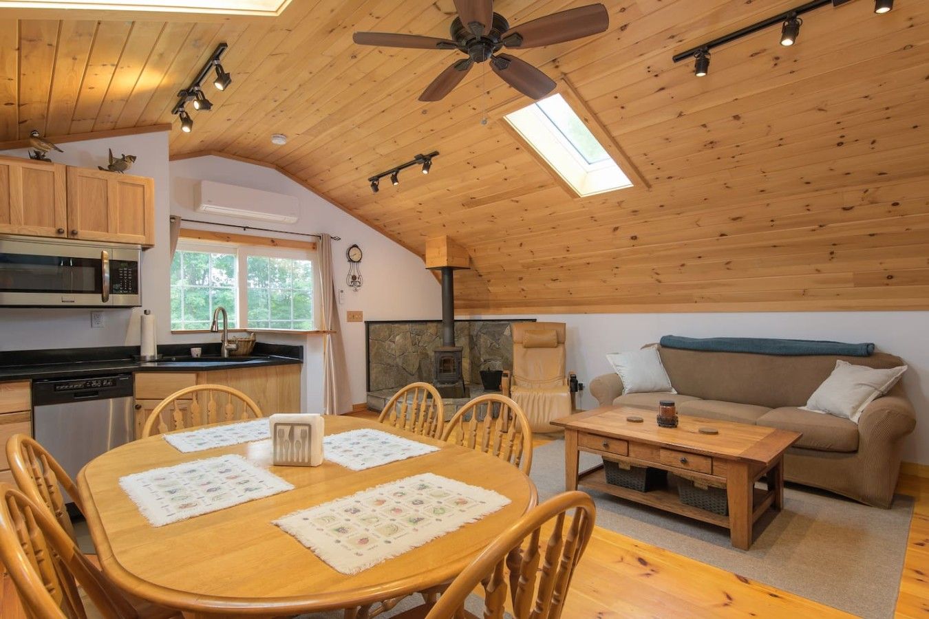 Ein gemütliches Blockhaus-Interieur mit Esstisch, Stühlen, einer Couch, einem Kamin und einem Deckenventilator.