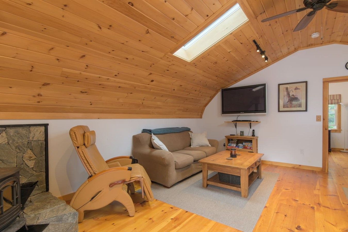 Une pièce chaleureuse avec un plafond en bois, un canapé, un fauteuil inclinable, une table basse et un téléviseur à écran plat.