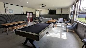 A pool table in a room with ceiling fans, a television, and seating areas.