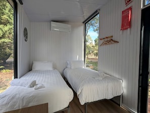 Une chambre avec deux lits, une fenêtre, une couverture anti-feu et un climatiseur fixé au mur.