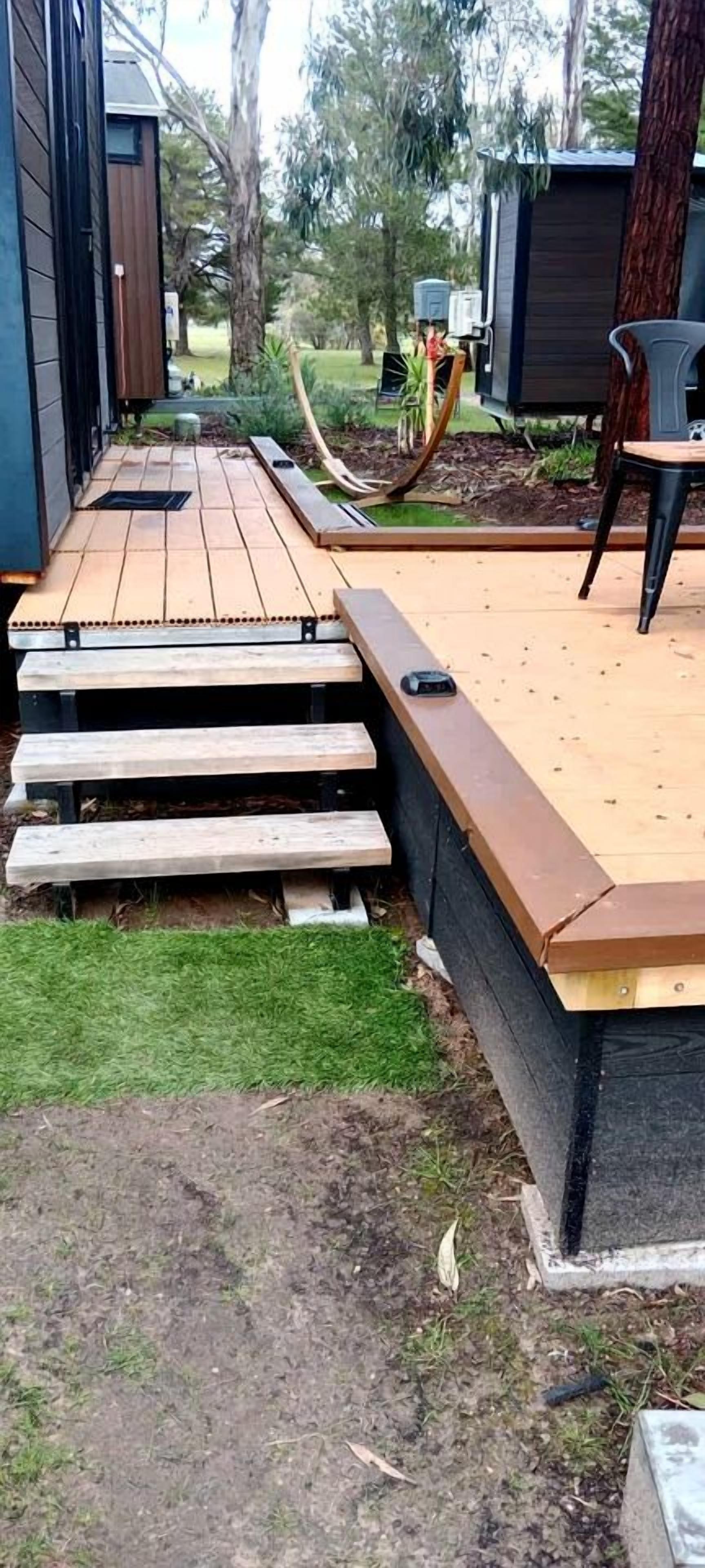 A deck with wooden steps leading to a raised platform, surrounded by a grassy area and trees.